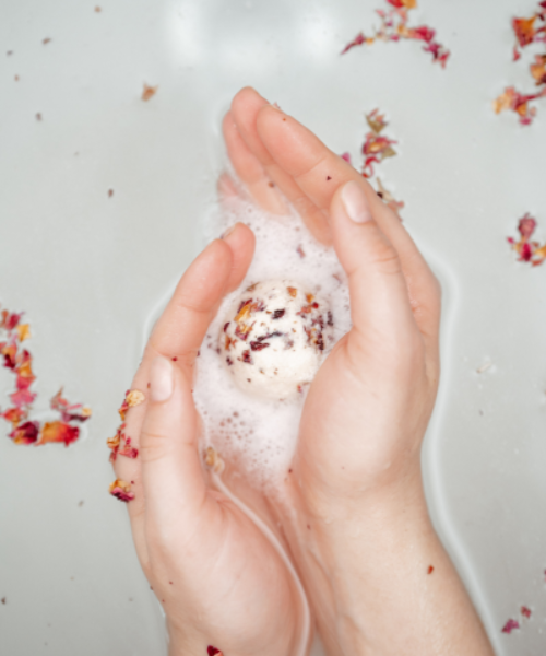 Natava hibiszkuszos fürdőgolyót tartó kéz fürdővízben