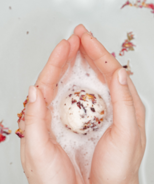 Natava fürdőgolyó kézben tartva egy kád fürdővízben